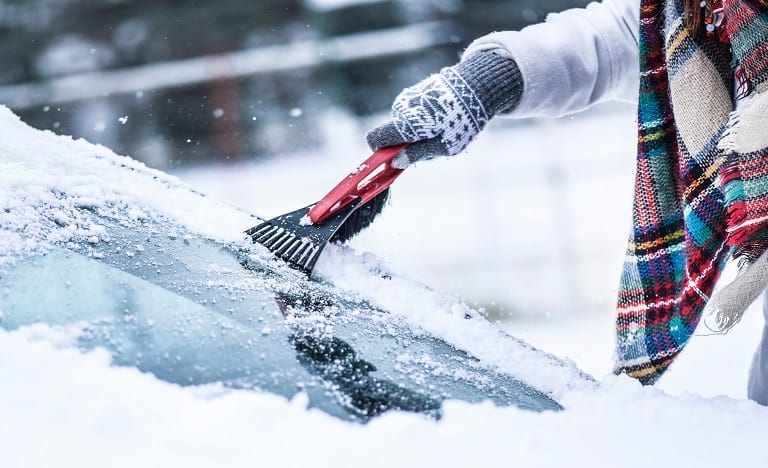 Woman using an ice scraper to remove ice and snow from her windshield